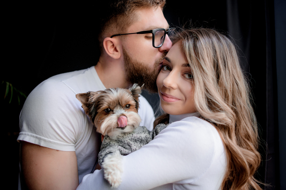 Man Kissing Woman On Side Of Face With Puppy In Between Them