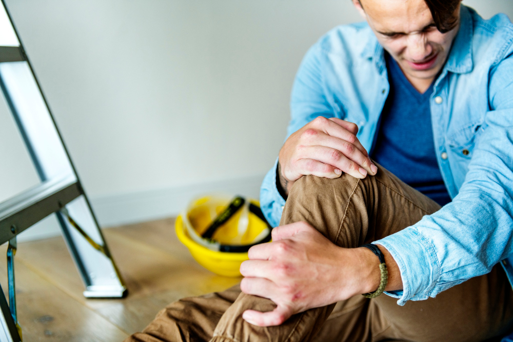 Male-With-Ladder-In-Background-Sitting-On-Floor-Clenching-Knee