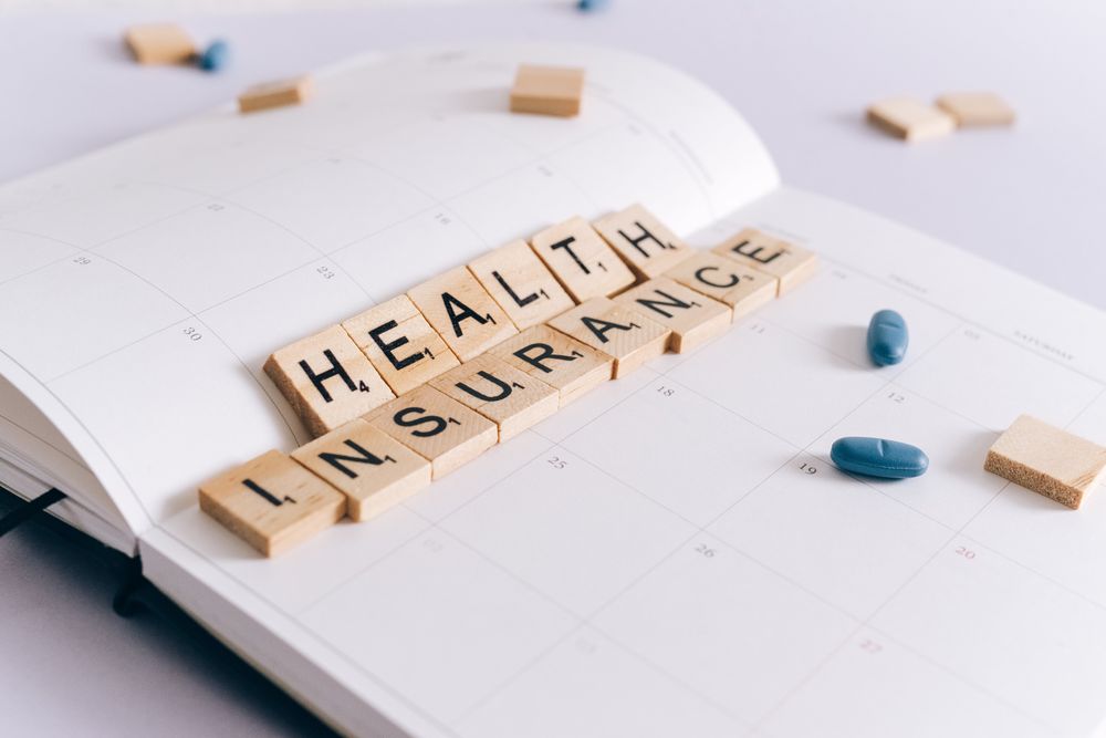 Open Notebook With Wood Letter Squares Spelling Health Insurance